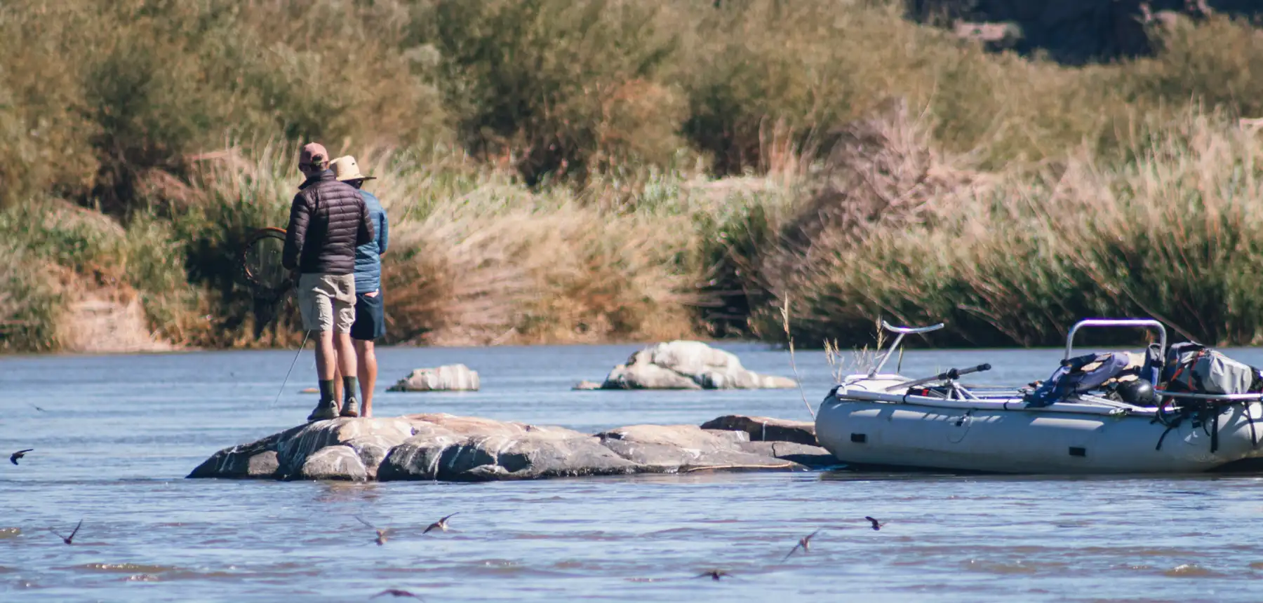 Two people fishing while standing on river rock