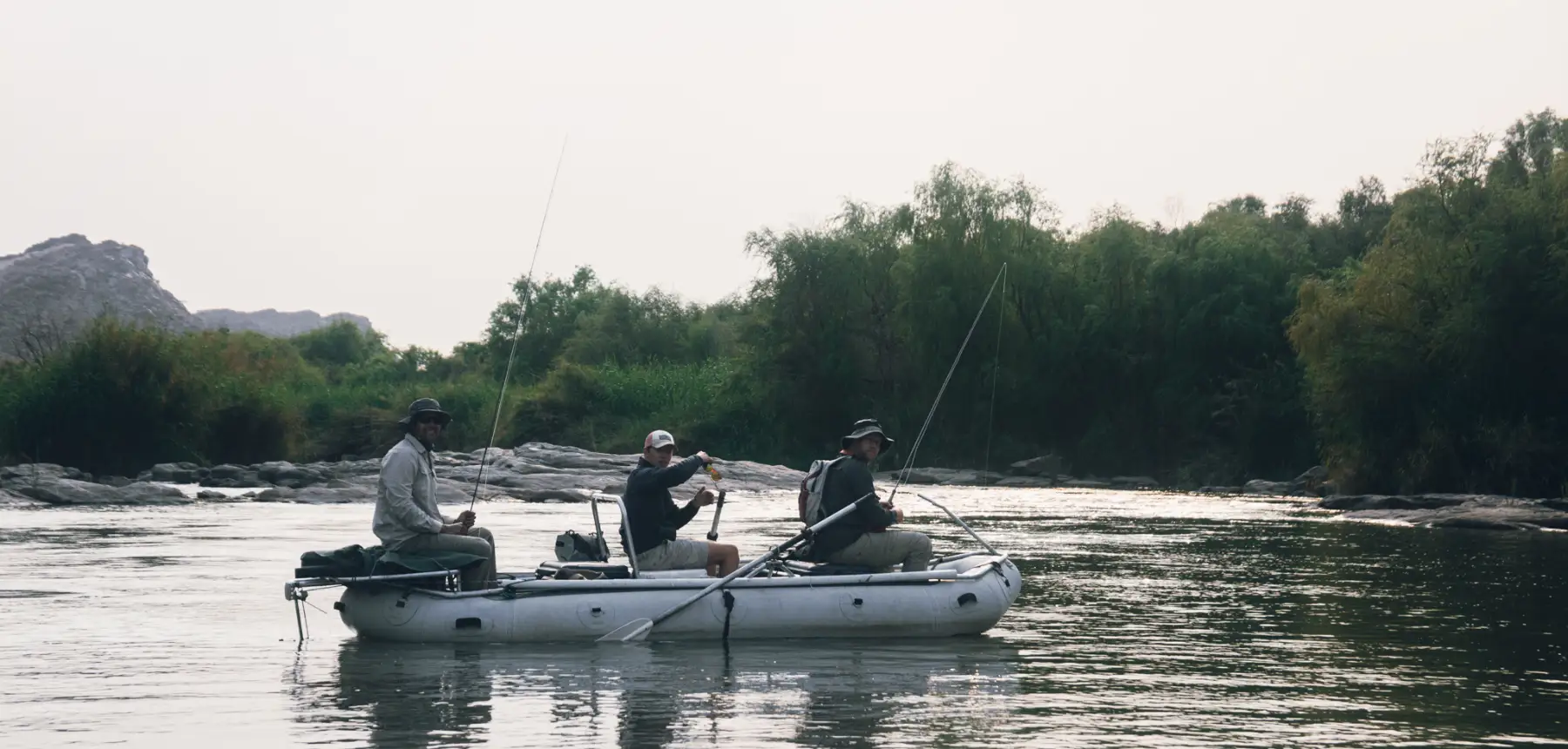 Three people fishing from inflatable raft on river