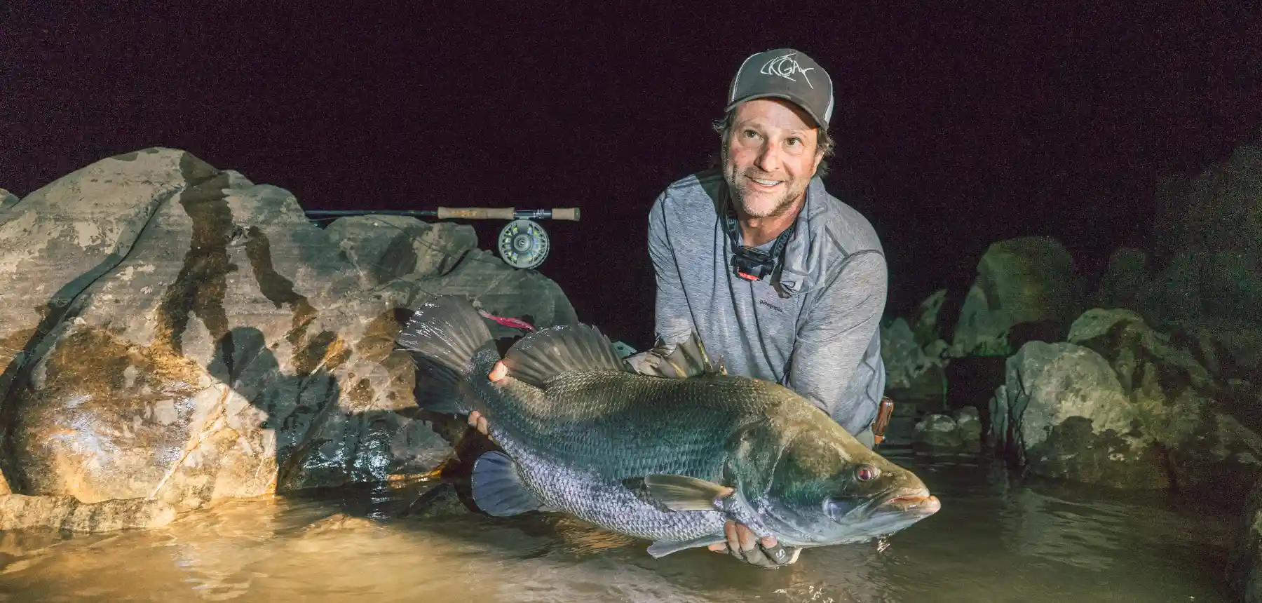 Man holding fish at night near rocks and water