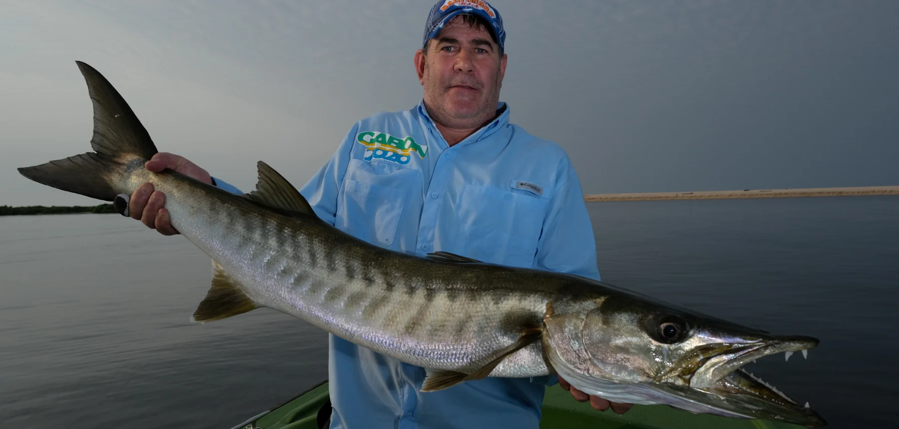 Man holding long barracuda on boat in open water