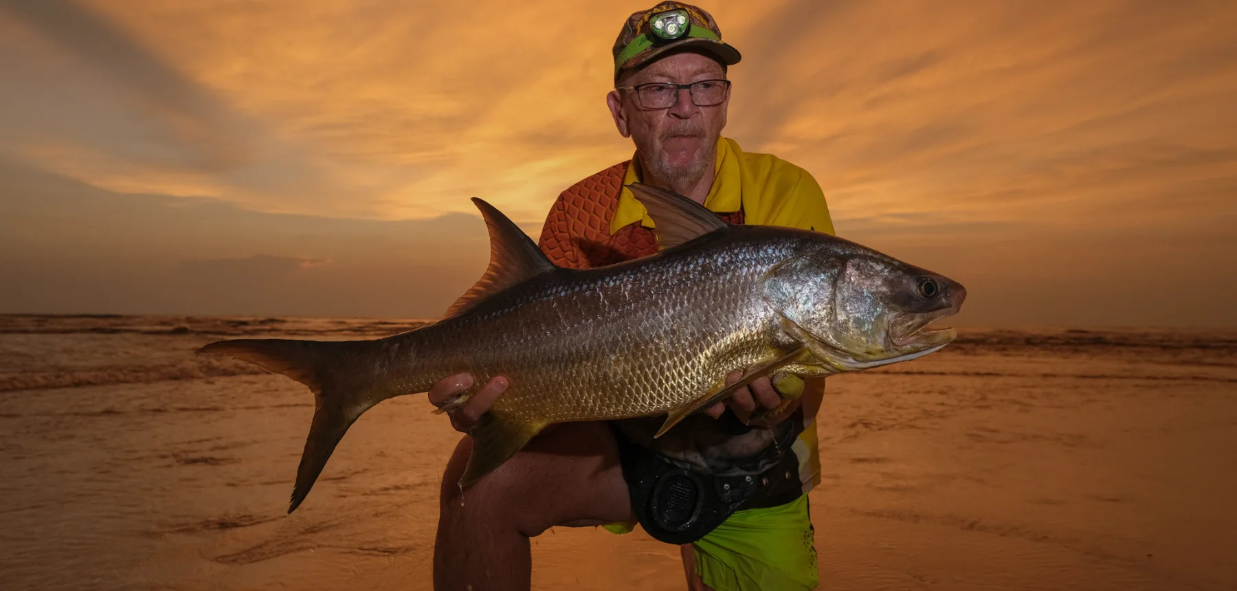 Man holding fish on beach at sunset