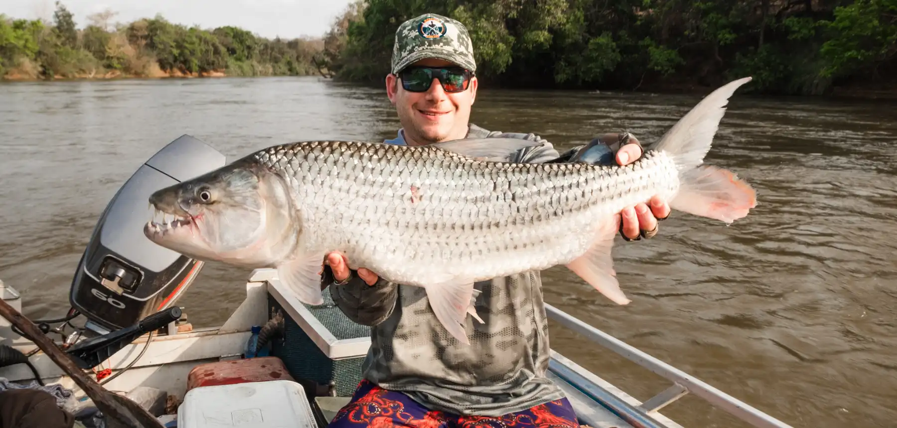 Man holding tigerfish while sitting on boat in river