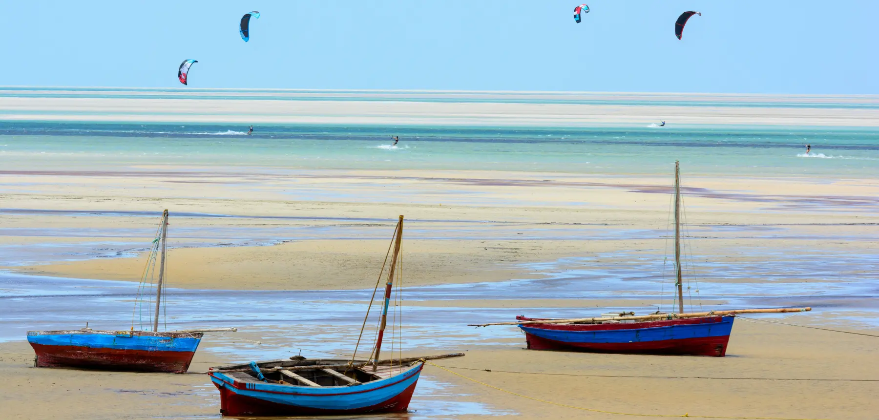 Traditional wooden boats on a shallow tropical lagoon with kitesurfers in the distance
