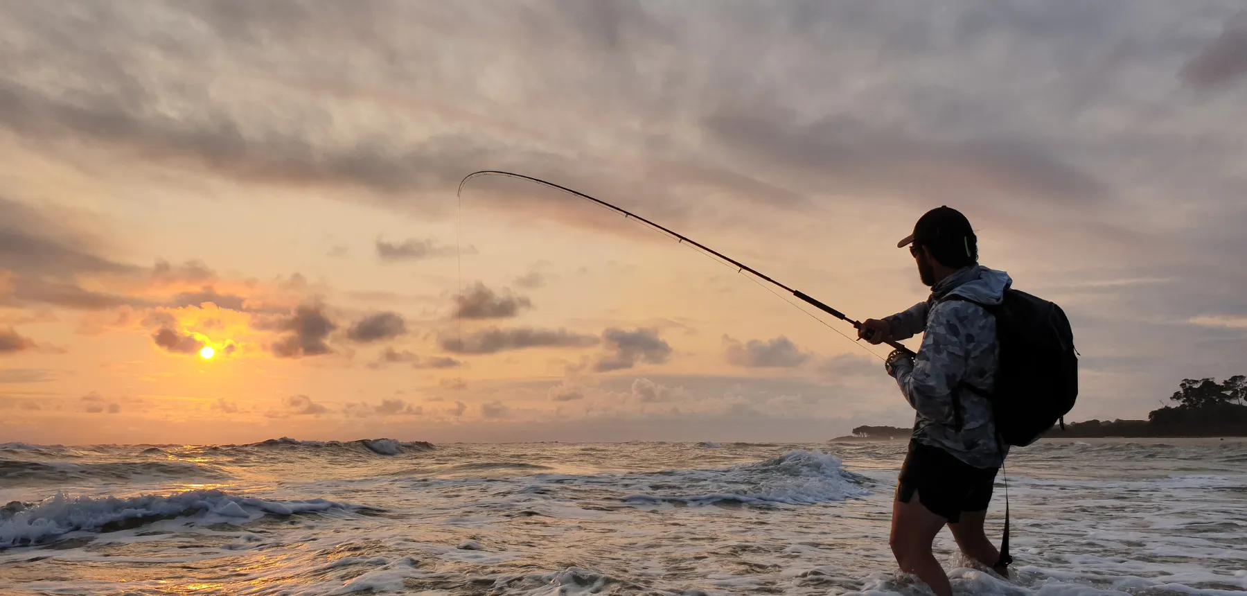 Person casting fishing rod into ocean at sunrise