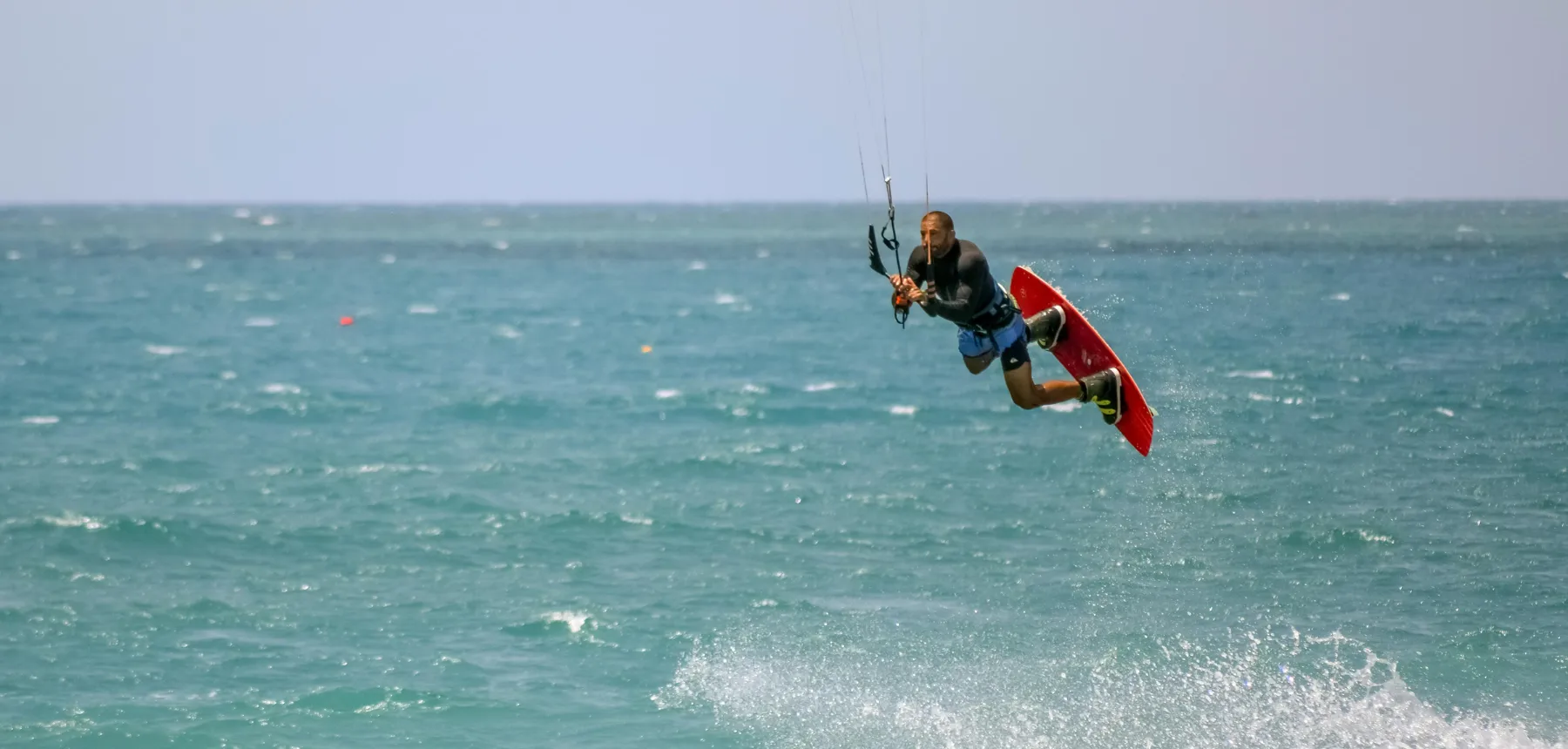 Kitesurfer jumping above ocean waves on a windy day with clear horizon
