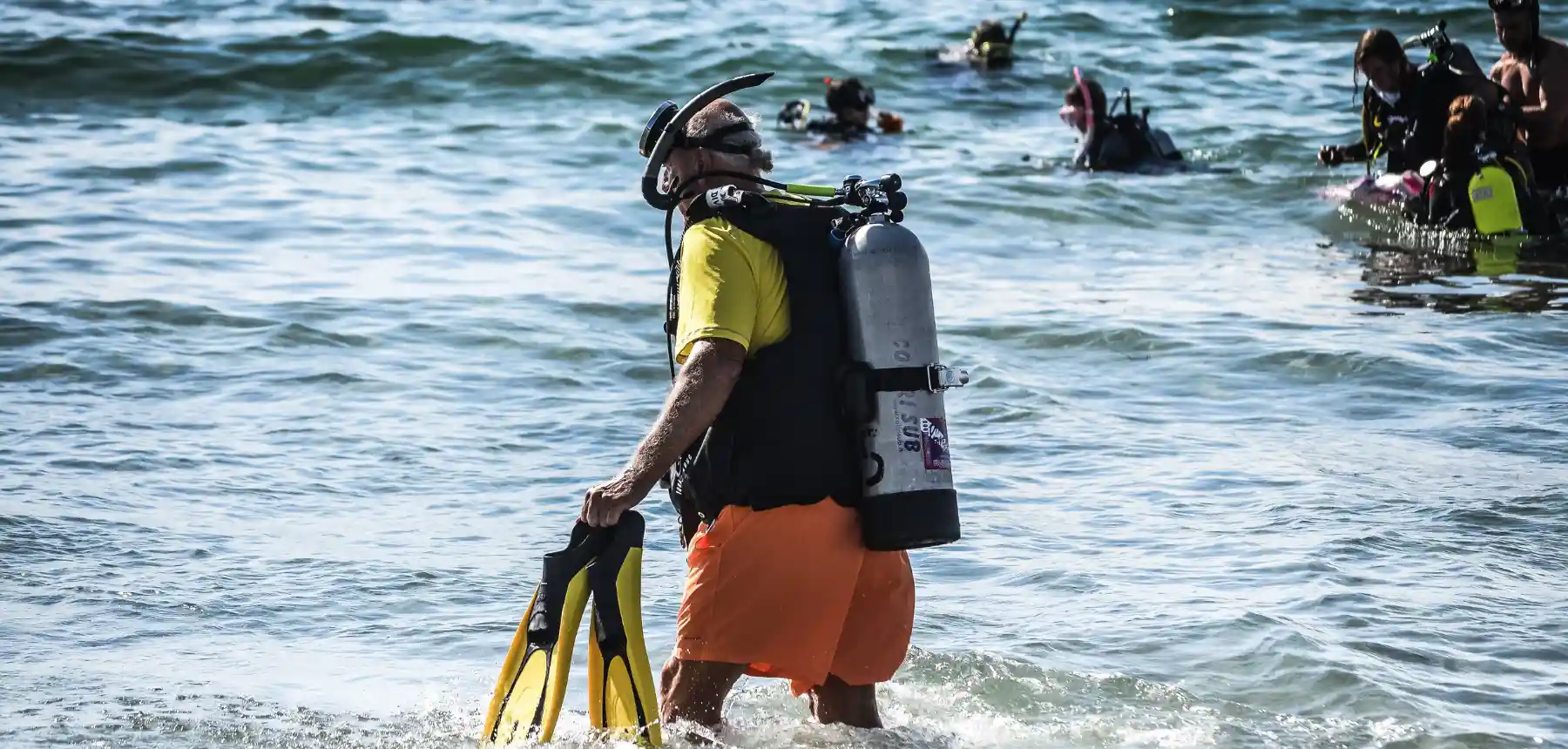 Scuba diver walking into the sea with equipment while group prepares behind