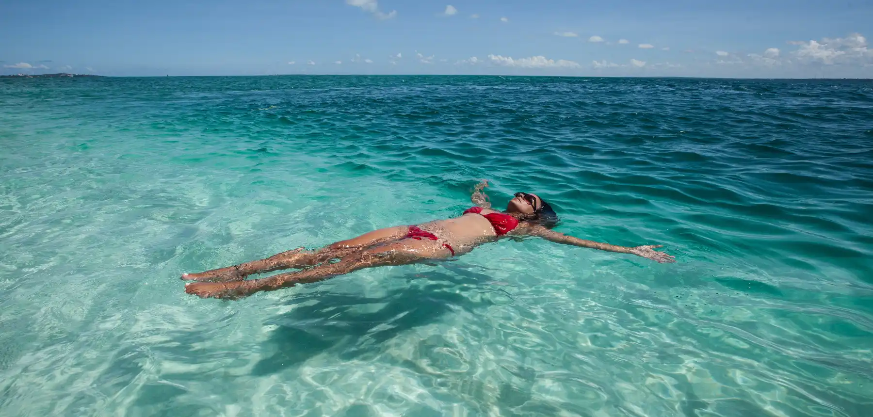 Woman floating in crystal clear turquoise ocean water on a tropical beach holiday