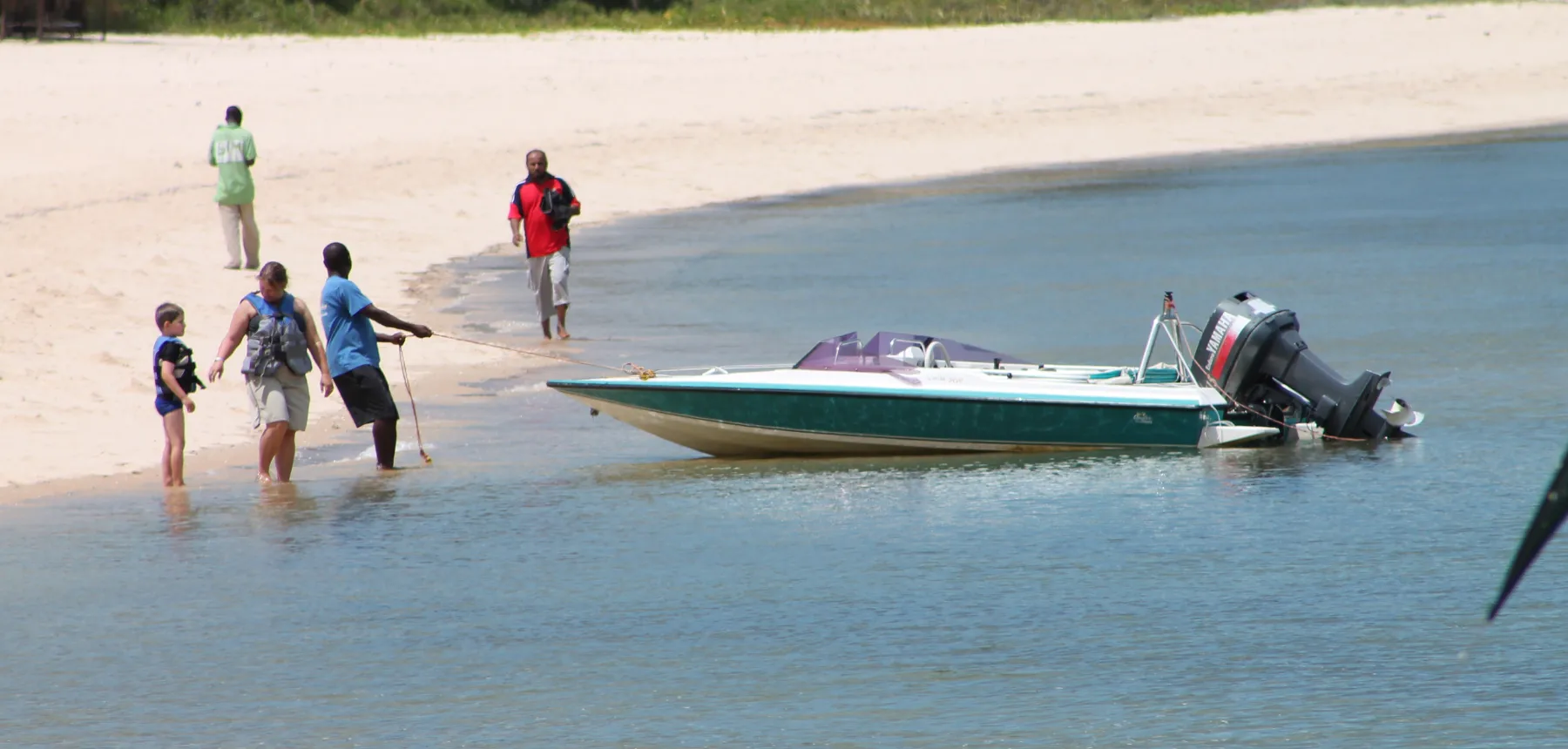 Local guide pulling a small boat ashore with a family on a quiet tropical beach