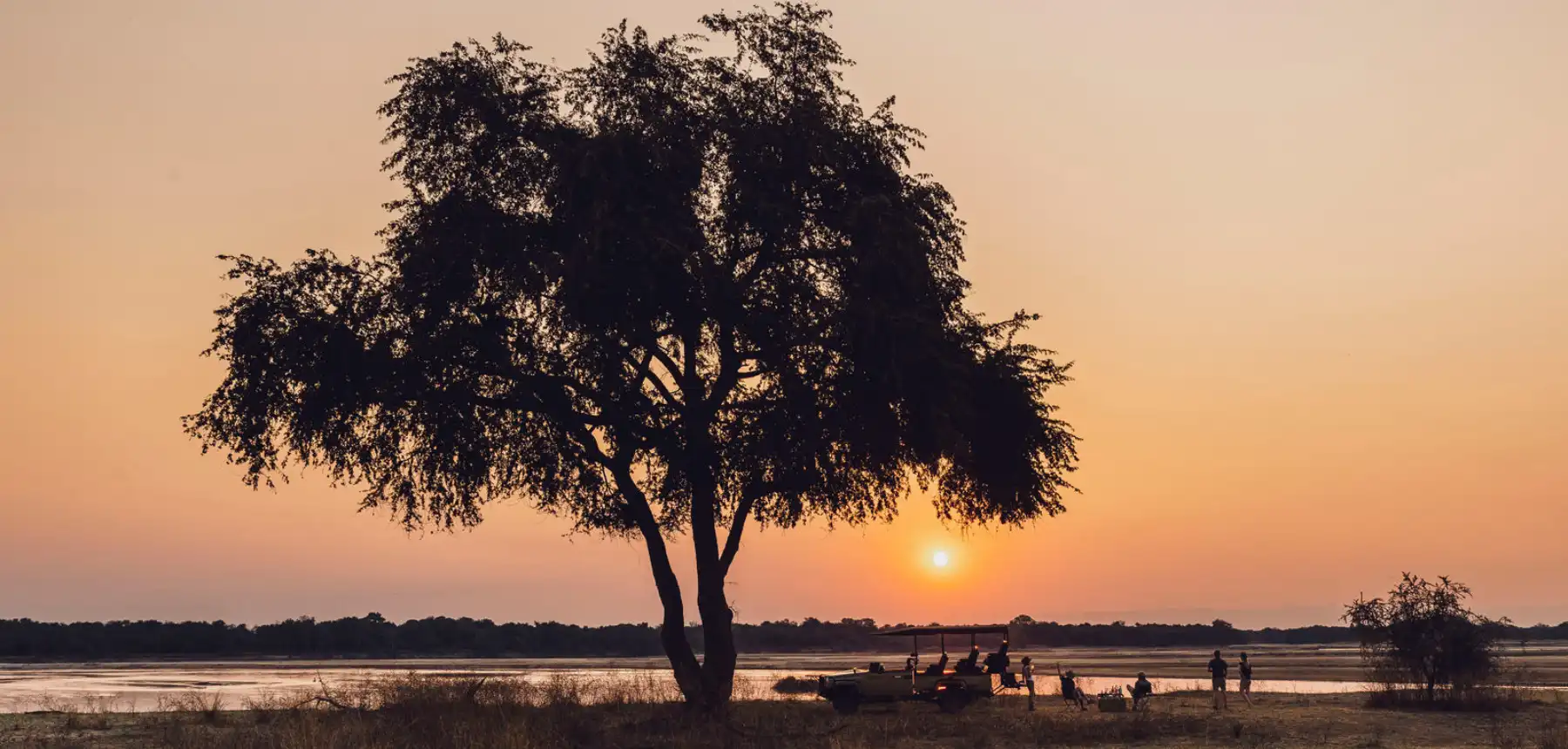 Safari sundowner scene beside a river at sunset with a tree silhouette in Africa