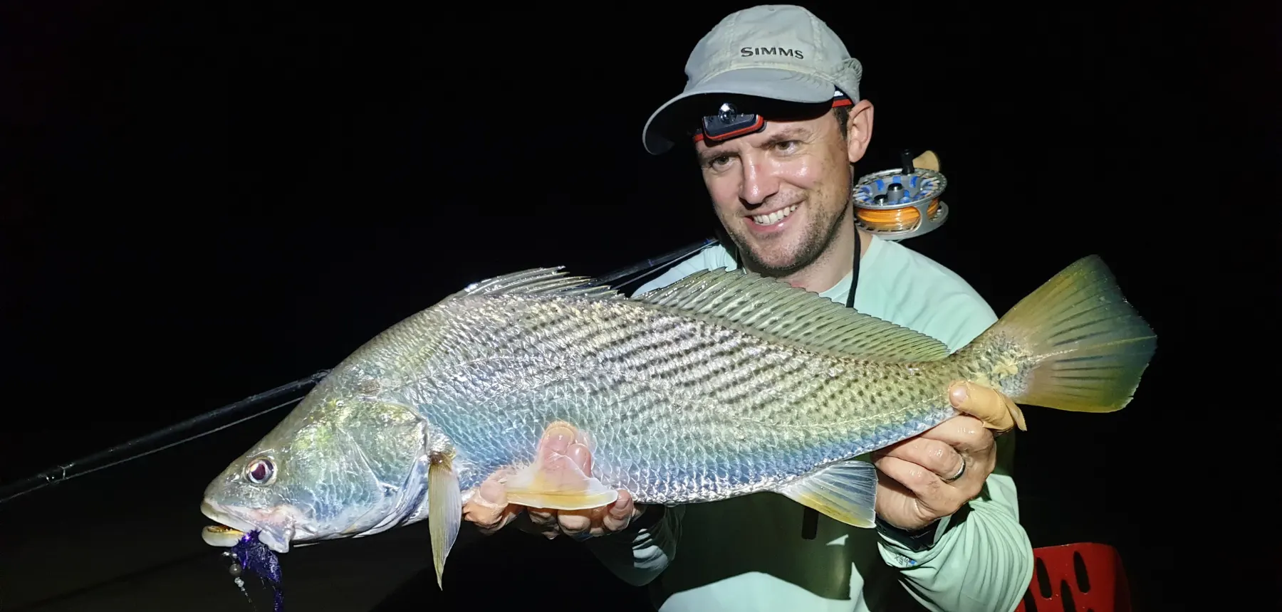 Man holding freshwater fish at night with dark background
