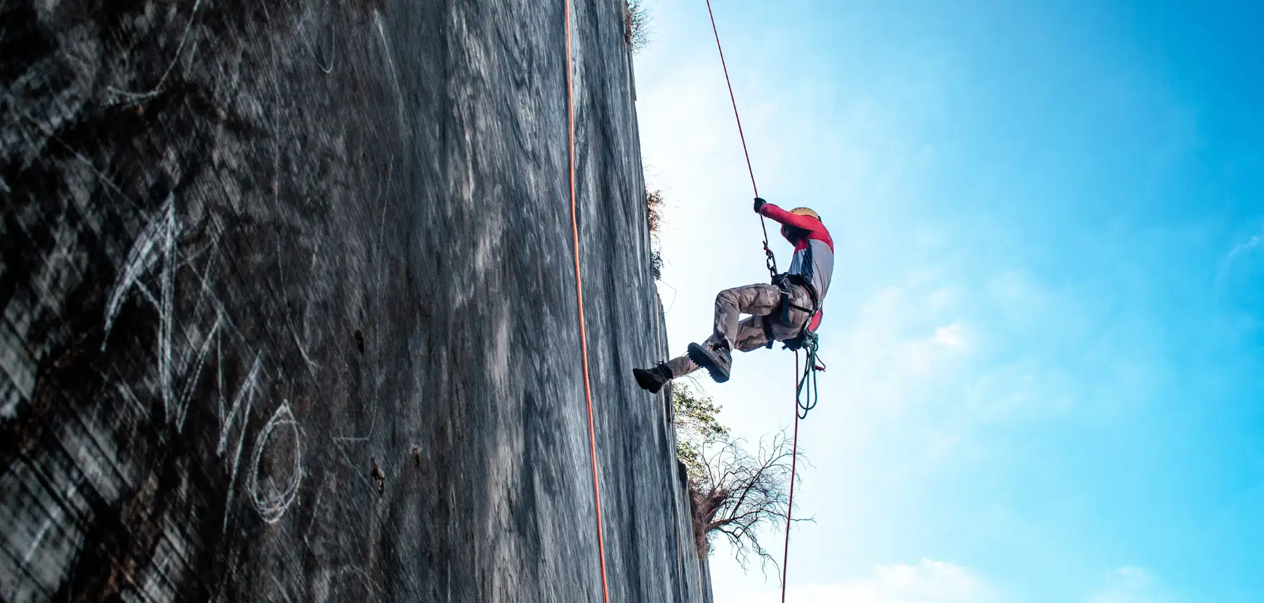 Person abseiling down steep rock face using rope and safety gear