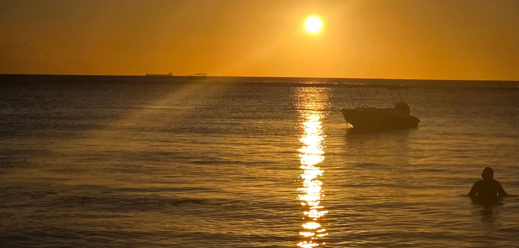 Golden sunset over the ocean with a boat silhouette reflecting on calm water